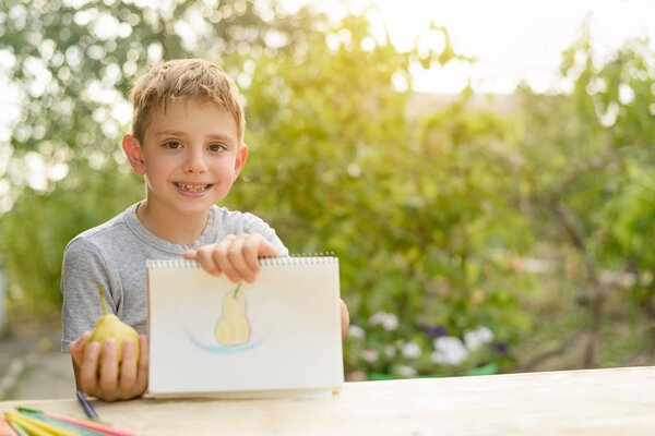 Cute boy shows drawn pear. Open air. Garden in the background. Creative concept.