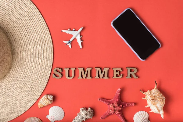 字夏天从木字母。贝壳，帽子的一部分，小飞机和智能手机，活珊瑚背景。平躺。旅行理念 — 图库照片