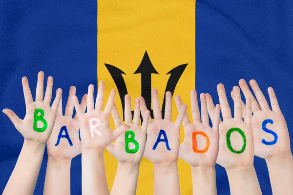 Надпись Барбадос на детских руках на фоне размахивающего флагом Барбадоса — стоковое фото