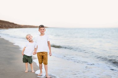 İki kardeş deniz kıyısında el ile yürürler. Aile tatili. Dostluk