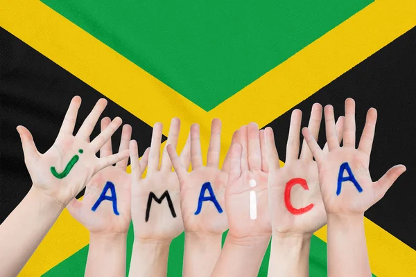 Надпись Ямайка на руках детей на фоне размахивающего флагом Ямайки — стоковое фото