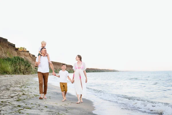 Familia de cuatro caminando por la orilla del mar. Padres y dos hijos. Familia amistosa feliz — Foto de Stock