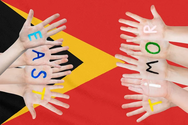 Inscripción Timor Oriental en las manos de los niños sobre el fondo de una bandera ondeante del Timor Oriental — Foto de Stock