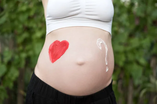 Czerwone serce i znak zapytania sporządzone na ciężarnej kobiecej brzuchu. Koncepcja w ciąży. Zbliżenie — Zdjęcie stockowe