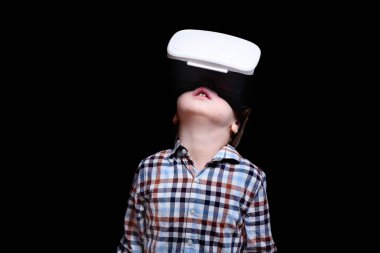 Sanal gerçeklik gözlüğü ile küçük sarışın çocuk bakar. Ekose gömlek. Siyah arka plan