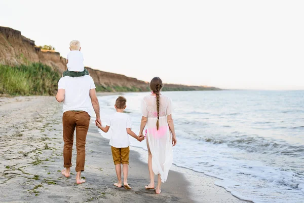 Familia de cuatro caminando por la orilla del mar. Padres y dos hijos. Vista trasera — Foto de Stock