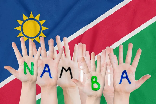 Inskription Namibia på barnens händer mot bakgrund av en viftande flagga av Namibia — Stockfoto