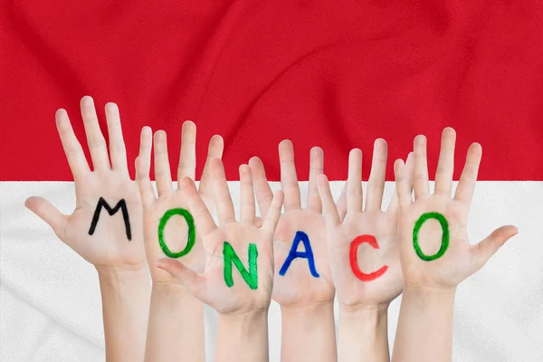 Напис Монако на руках дітей на тлі розмахуючи прапором Монако — стокове фото