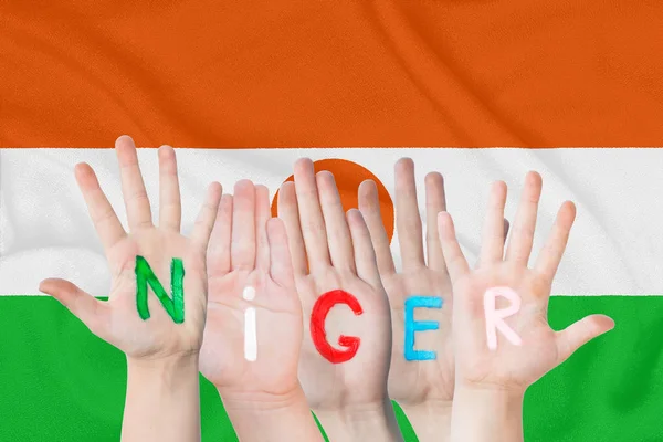 Inscripția Niger pe mâinile copiilor pe fundalul unui steag de fluturare al Nigerului — Fotografie, imagine de stoc