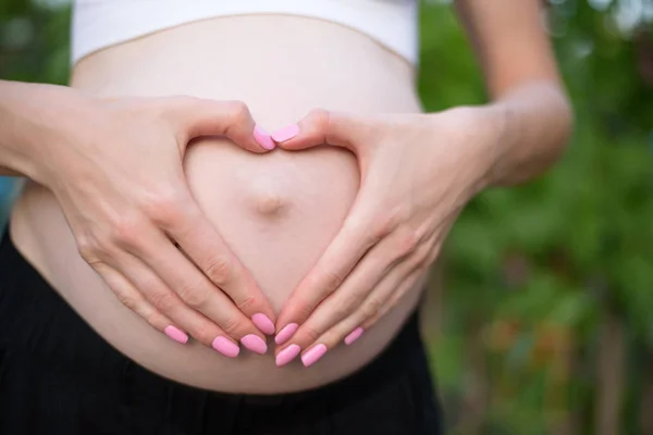 Manos femeninas en forma de corazón en su vientre. Concepto de embarazada. Primer plano — Foto de Stock