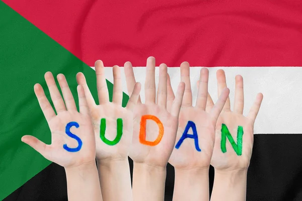 Inschrift sudan auf den Händen der Kinder vor dem Hintergrund einer schwenkenden Fahne des sudan — Stockfoto