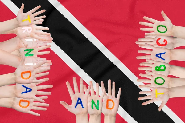 Надпись на руках детей Тринидада и Тобаго на фоне размахивающего флагом Тринидада и Тобаго — стоковое фото