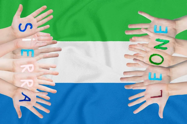 Inscripción Sierra Leona en las manos de los niños sobre el fondo de una bandera ondeante de Sierra Leona — Foto de Stock