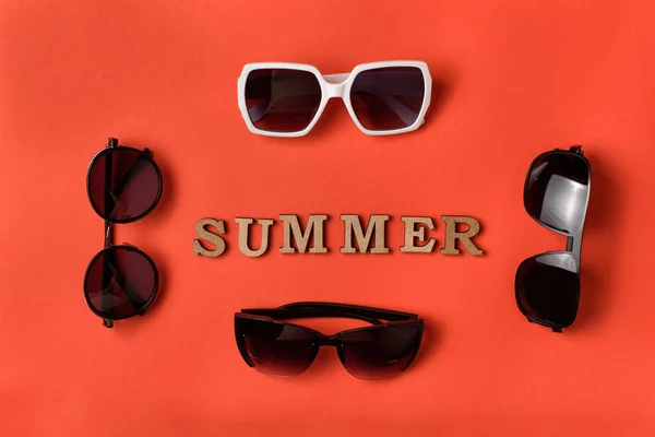 Palabra de verano de letras de madera. Cuatro gafas de sol sobre fondo de coral vivo. Concepto de viaje —  Fotos de Stock