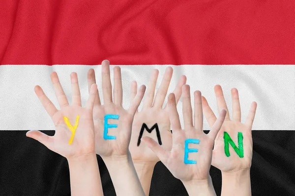Inscripción Yemen en las manos de los niños en el contexto de una bandera ondeante del Yemen — Foto de Stock