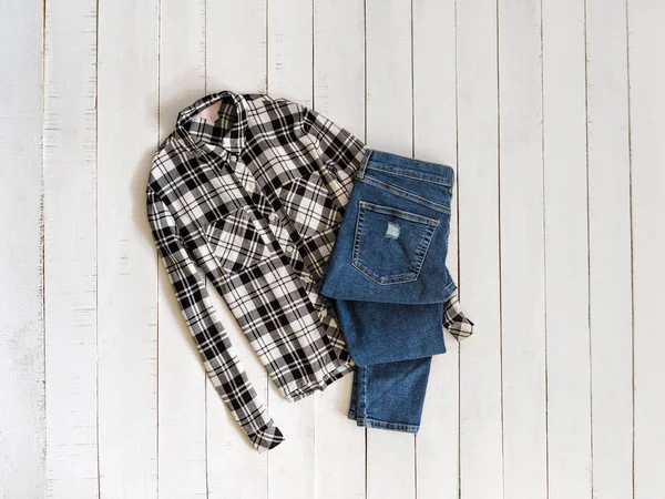 Black and white checkered shirts and jeans on a wooden background. Top view — Stock Photo, Image