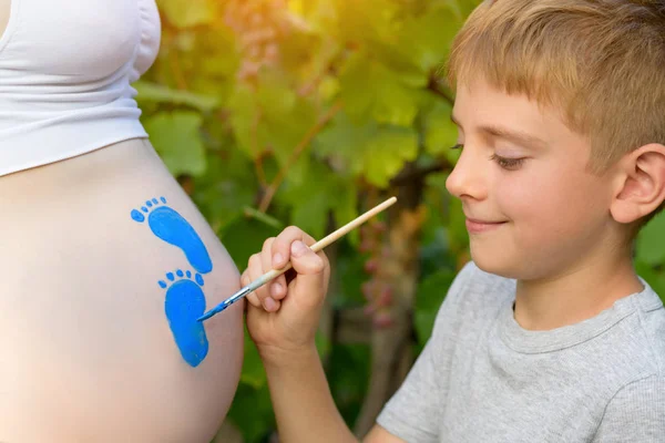 Mały chłopiec rysuje z pędzlem na brzuchu jego ciąży mama dziecka ślad. Koncepcja w ciąży. Zbliżenie — Zdjęcie stockowe