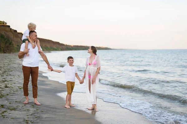 Familia de cuatro caminando por la orilla del mar. Padres y dos hijos. Familia amistosa feliz — Foto de Stock