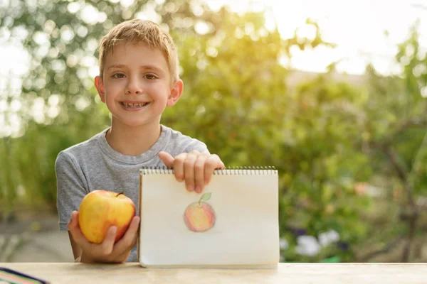 Cute boy shows drawn apple. Open air. Garden in the background. Creative concept.