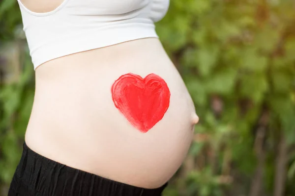 Corazón rojo dibujado en el vientre de una mujer embarazada. Concepto de embarazada. Primer plano — Foto de Stock