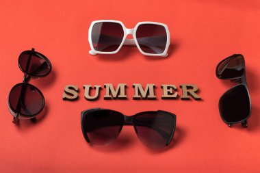 Tahta harflerden Kelime Yaz. Canlı mercan arka planında dört güneş gözlüğü. Seyahat konsepti