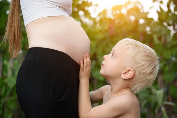 Le petit garçon blond caresse le ventre de sa mère enceinte. Concept de famille — Photo