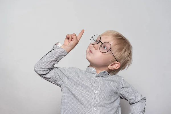 Portrait d'un mignon garçon blond avec de grandes lunettes. Le doigt pointant vers le haut. Fond blanc . — Photo