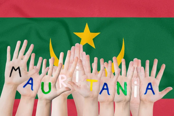 Inscripción Mauritania en las manos de los niños sobre el fondo de una bandera ondeante de Mauritania — Foto de Stock