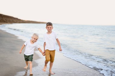 İki kardeş deniz kıyısında el ile yürürler. Aile tatili. Dostluk