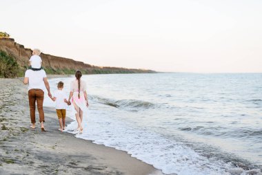 Deniz kıyısında yürüyen dört kişilik bir aile. Ebeveynler ve iki oğlu var. Geri görünüm