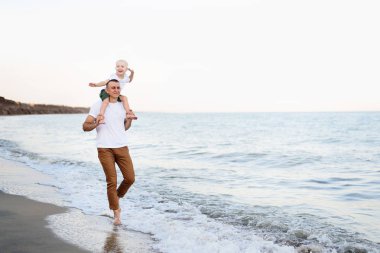 Omuzlarında sarışın bir oğlu olan baba deniz kıyısında yürüyor. Aile tatili