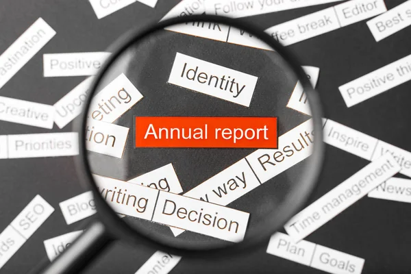 Magnifier glass over the red inscription annual report cut out of paper. Surrounded by other inscriptions on a dark background. Word cloud concept. — Stock Photo, Image