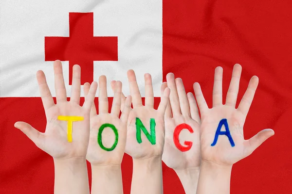 Inskription Tonga på barnens händer mot bakgrund av en viftande flagga av Tonga — Stockfoto