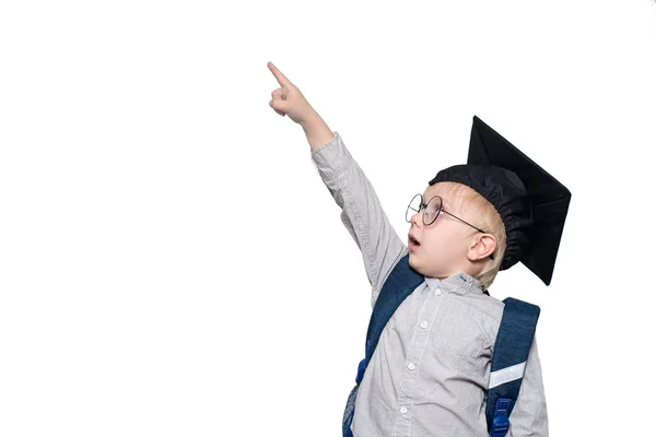 Surprised schoolboy in a suit, glasses and an academic hat points his finger up. School concept. Isolate — Stock Photo, Image