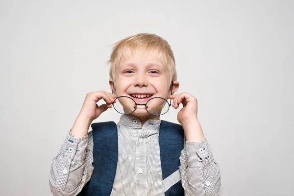 Portret van een schattige blonde school jongen rechtzetten glazen. School Bureau en schooltas. Witte achtergrond. — Stockfoto