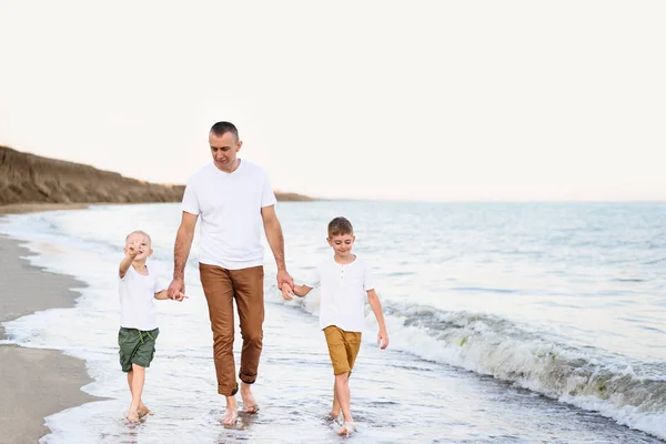 Padre y dos hijos caminan por la orilla del mar. Disfrutando de las vacaciones — Foto de Stock