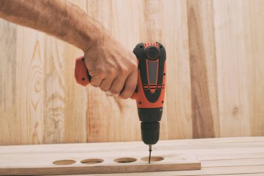 Erkek elinde elektrikli matkap tornavida. Açık kahverengi ahşap masa üzerinde iş parçası işleme, vida sıkma.