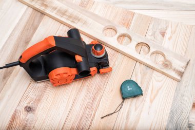 Elektrikli düzlem, ölçüm bandı ve iş parçası açık kahverengi ahşap bir masa üzerinde yatıyor. Ahşap.