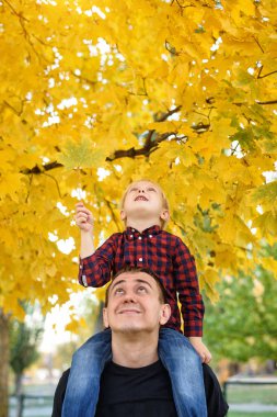 Ekose gömlekli sarışın çocuk babasının omuzlarında oturuyor. Yukarı bak. Sonbahar konsepti