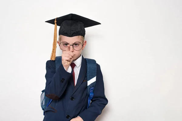 Poważny uczeń w garniturze, okulary i kapelusz akademicki punktów palcem. Koncepcja szkoły. Białe tło. — Zdjęcie stockowe