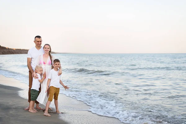 Familia feliz de cuatro abrazos en la costa del mar. Padres, madre embarazada y dos hijos . — Foto de Stock