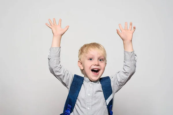 Retrato de un alegre colegial rubio con una bolsa de escuela. Manos arriba. Fondo blanco . — Foto de Stock