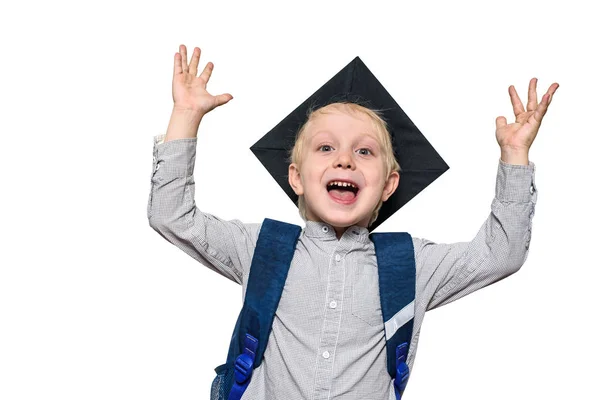 Retrato de un niño rubio alegre con sombrero académico y una bolsa de la escuela. Manos arriba. Aislar — Foto de Stock