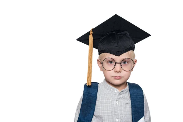Portrait d'un mignon garçon blond dans de grandes lunettes, chapeau académique et un sac d'école. Fond blanc. Place pour le texte — Photo
