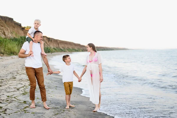 Family of four walking along the seashore. Parents and two sons. Happy friendly family