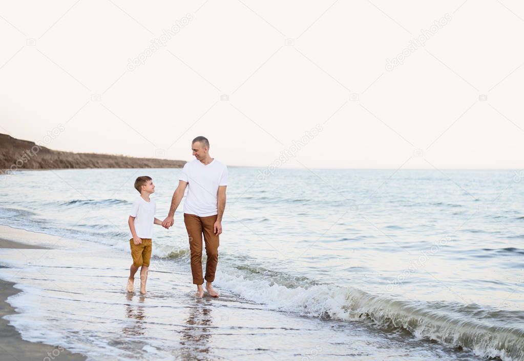 Father and son go by the hand along the sea coast. Family vacation. Friendship