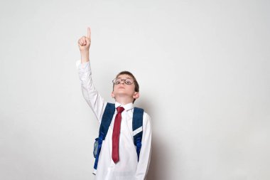 Bir sırt çantası ve yuvarlak gözlük ile çocuk parmağını yukarı puan. Okul konsepti. Beyaz arka plan.