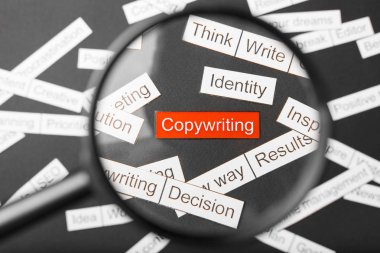 Kırmızı yazıt üzerinde büyüteç cam kağıt kesilmiş copywriting. Karanlık bir arka planda diğer yazıtlar ile çevrilidir. Word bulut konsepti.