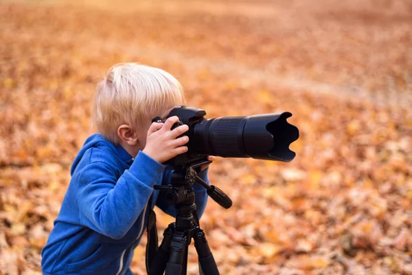 Malý blonďák fotografuje na SLR kameře. Podzimní Park — Stock fotografie