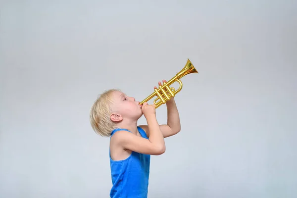 Pouco bonito menino loiro tocando trompete de brinquedo no fundo de luz — Fotografia de Stock